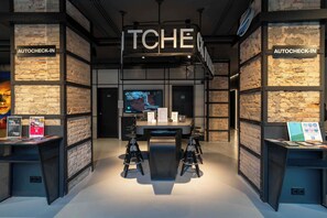 Een modern interieur met een centrale tafel, barstoelen en borden met de tekst 'AUTOCHECK-IN' aan weerszijden.