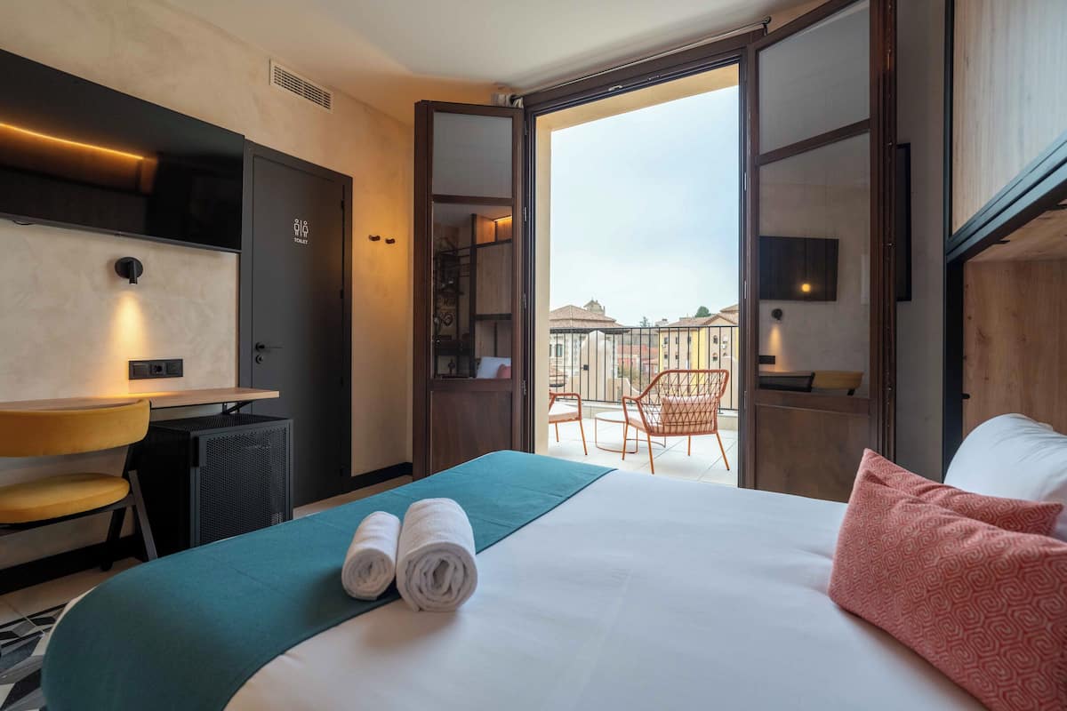 Une chambre d’hôtel comprenant un lit, un bureau, une chaise et un balcon avec des chaises.