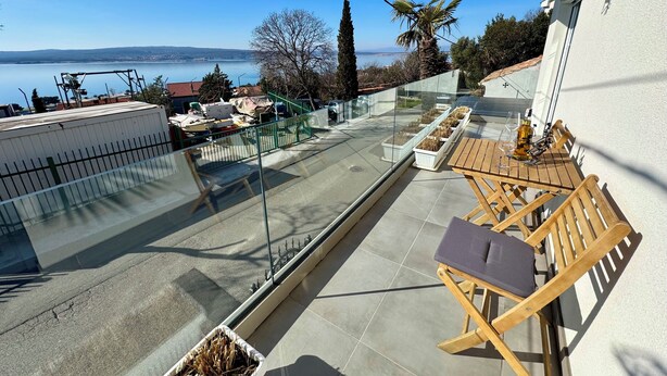 A balcony with a view of a lake, a table with chairs, and potted plants. - Apartment Toma 1 (Crikvenica)