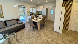 A modern living room with a sofa and a glass coffee table, a dining area with a table set for four, and a kitchen with white cabinets and a refrigerator. - Apartment Toma 1 (Crikvenica)