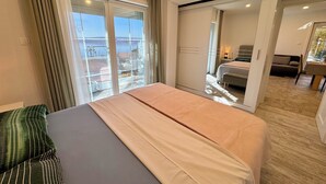 A hotel room with a bed, a sofa, a large window with curtains, and a view of the outside. - Apartment Toma 1 (Crikvenica)
