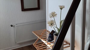 Een trap met een houten leuning, een witte radiator en een houten schoenenrek met een paar schoenen en een vaas met bloemen.