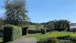 Een verhard pad dat leidt naar een landelijk gebouw met een rieten dak, omgeven door weelderige begroeiing en een heldere blauwe lucht.