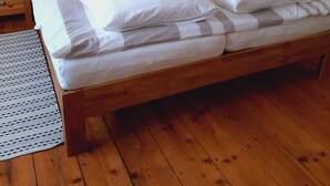 Een netjes opgemaakt bed met een gestreept dekbed en kussens, een houten garderobe, een ingelijst kunstwerk aan de muur en een houten vloer.