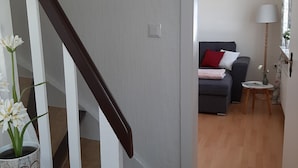 Een trap met een witte leuning die leidt naar een woonkamer met een grijze bank, een klein tafeltje en een vloerlamp.