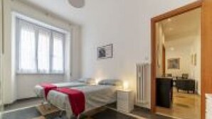 Ein Schlafzimmer mit einem Bett, einem Nachttisch, einem Fenster und einer Tür zu einem anderen Raum.