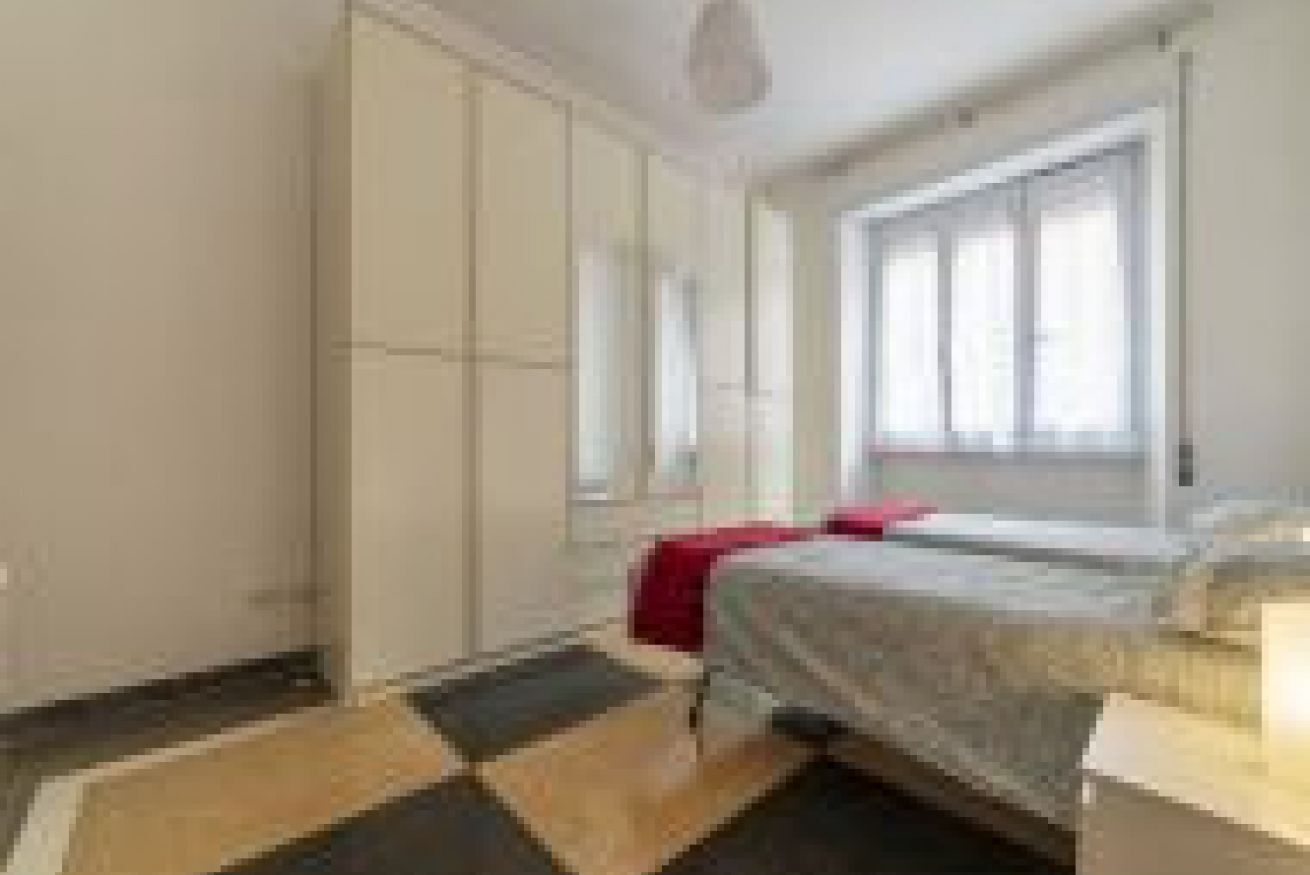 A bedroom with a bed, a window, a wardrobe, and a door.