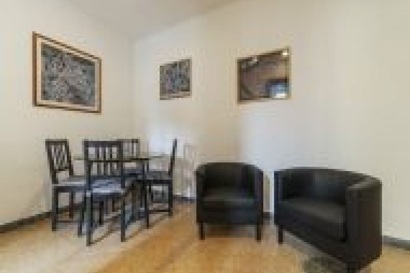 A room with a dining table and chairs, a black armchair, and framed artwork on the wall.