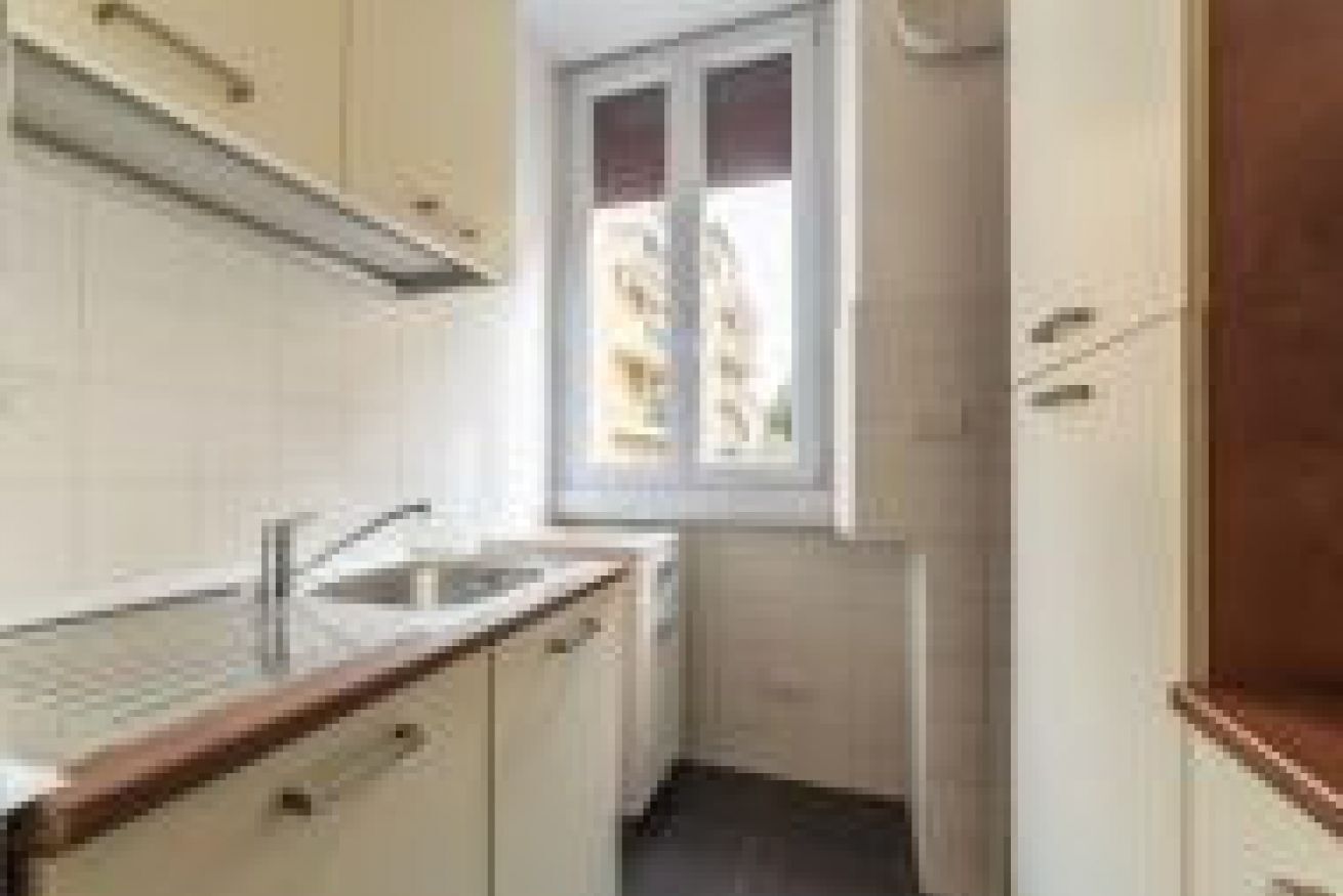A narrow kitchen with a window, white cabinets, and a wooden countertop.