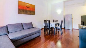 A living room with a sofa, a dining table with chairs, a refrigerator, and a TV stand. - GuestHost - Porto Antico Apartment (Genova)