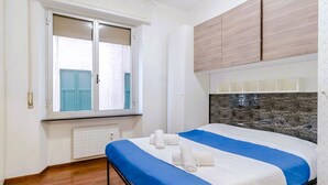 A bedroom with a bed, a window with shutters, a radiator, and wooden cabinets. - GuestHost - Porto Antico Apartment (Genova)
