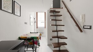 Eine Treppe mit Holzbalken, ein Essbereich mit Tisch und Stühlen sowie gerahmte Bilder an der Wand.