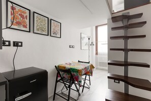 A dining area with a table covered in a floral tablecloth, a black coffee machine, and framed botanical prints on the wall.
