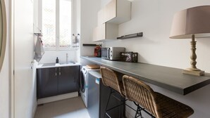 A compact kitchen with a washing machine, a microwave, and a bar stool.