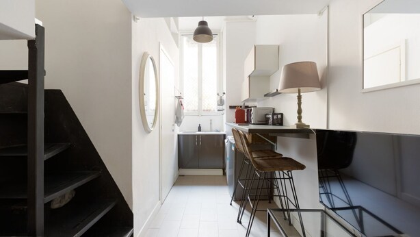 A compact kitchen with a dining area, a staircase, and a window providing natural light.