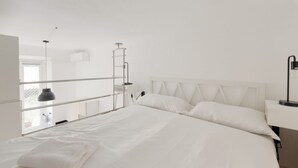 A white room with a bed, a desk, and a window.