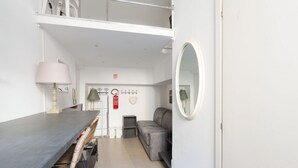 A modern room with a dining table, a sofa, a mirror, and a ceiling fan.