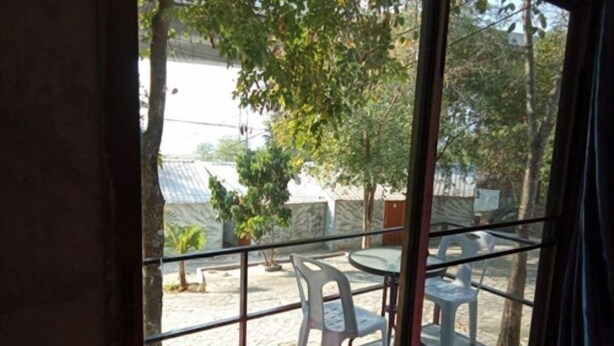 Un balcón con baranda de vidrio, mobiliario exterior y vista a una zona residencial con árboles y casas.