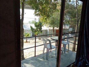 Un balcón con baranda de vidrio, mobiliario exterior y vista a una zona residencial con árboles y casas.