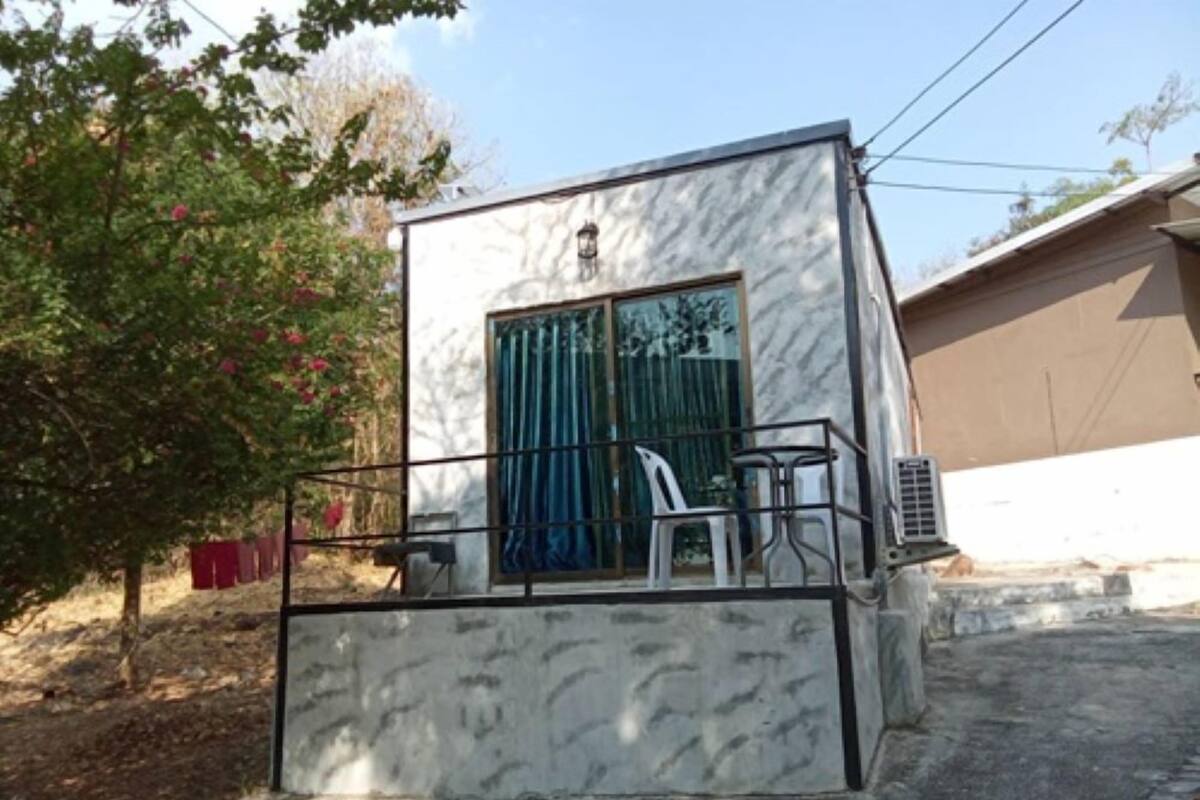 Un edificio pequeño de una sola planta con un balcón, una ventana con cortinas azules y una silla.