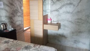 Habitación de hotel con cama, mesita de noche con hervidor, estante pequeño con espejo y pared con diseño de paneles de madera.