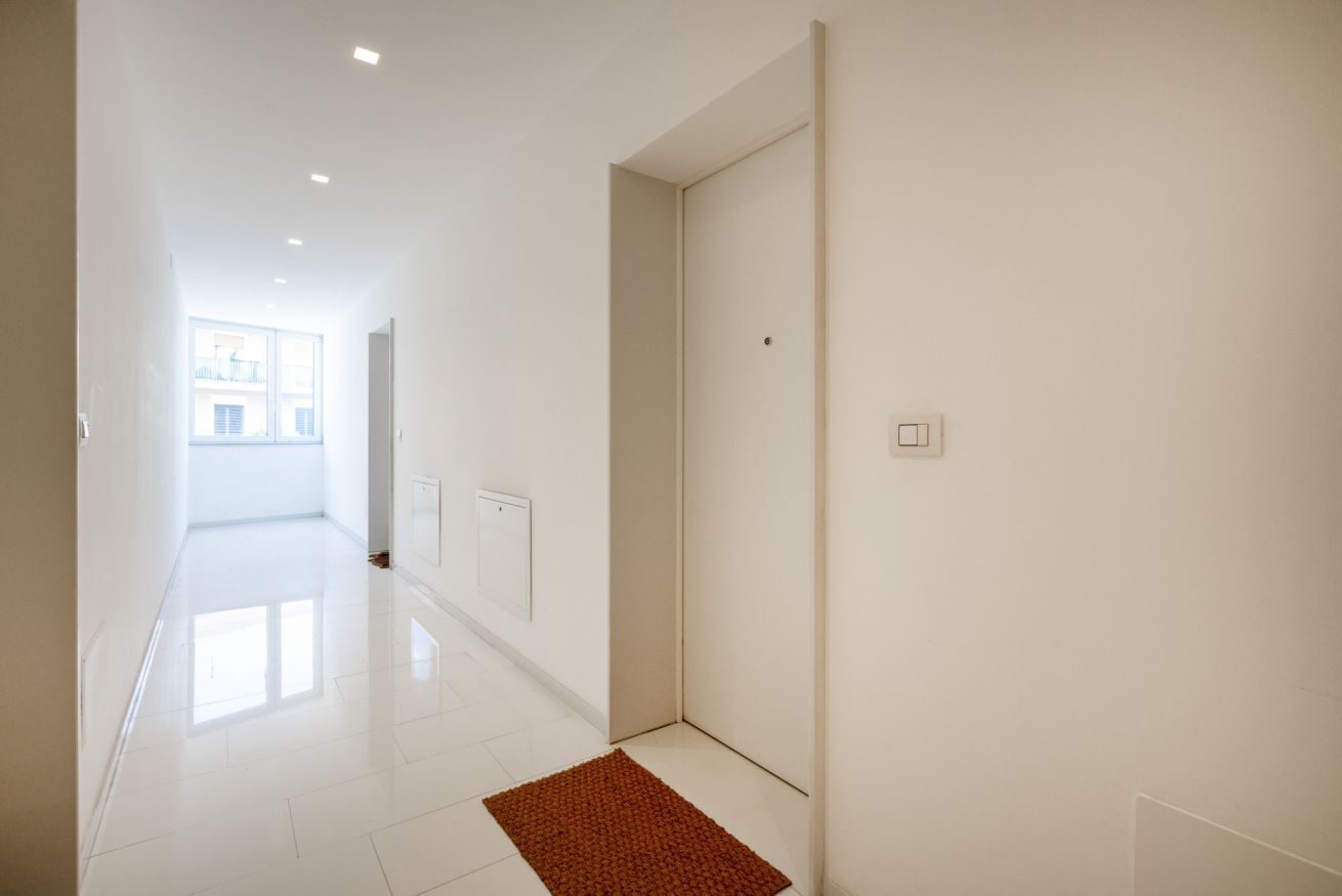 Een gang met witte muren, een rode mat en een deur naar een andere kamer.
