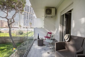 A balcony with a wicker chair, a red chair, and a wicker ottoman.