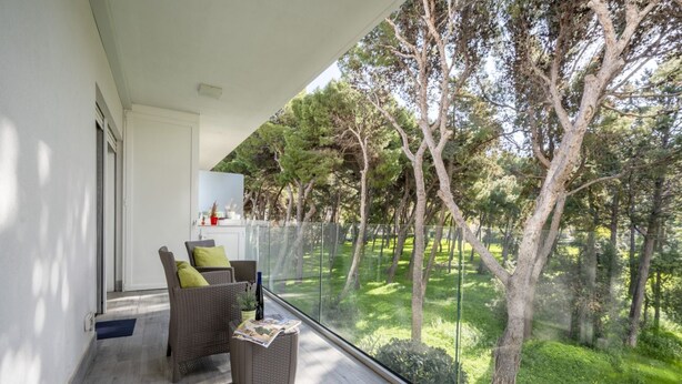 Un balcon doté de meubles en osier et d’une porte vitrée donnant sur un jardin arboré.
