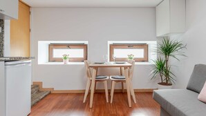 Et lille, moderne køkken med spiseplads, to vinduer med planter og en grå sofa.