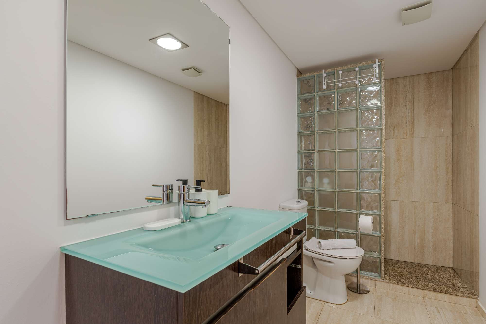 A modern bathroom with a glass sink, a toilet, and a shower with glass panels.