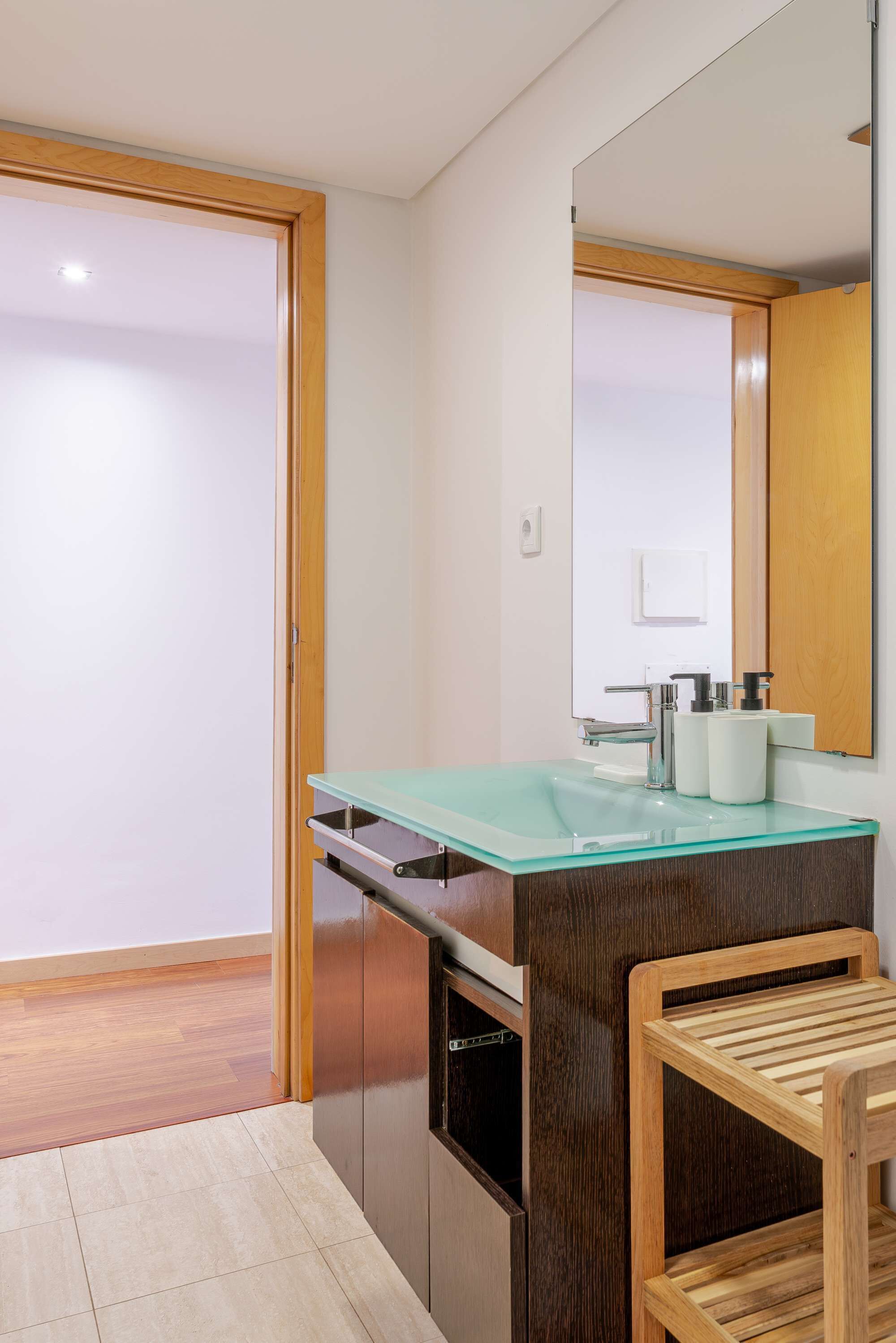 A modern bathroom with a glass sink, wooden cabinet, and a mirror.