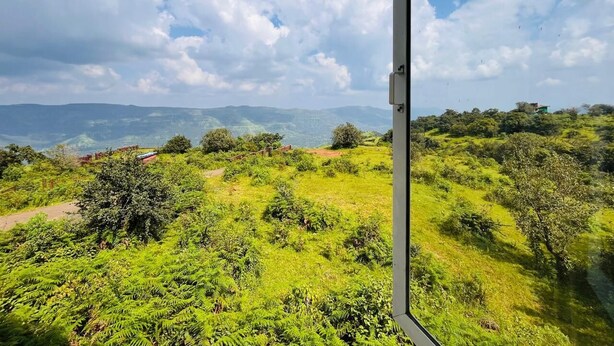 Blick aus einem Fenster auf eine üppige, grüne Landschaft mit sanften Hügeln und blauem Himmel.