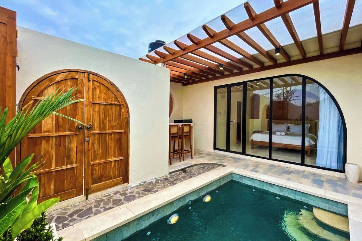 A pool area with a wooden door, a glass-enclosed bedroom, and a stone-tiled floor.