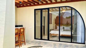 A bedroom with a curved glass door, a bed, and a small table with chairs. - Esha Private Pool Villas by AGATA (Ungasan)