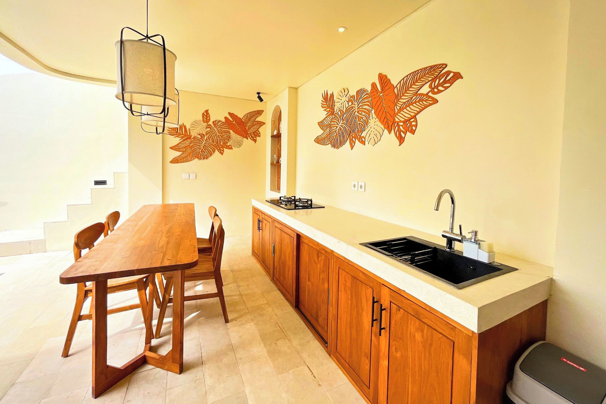 A modern kitchen with wooden cabinets, a large island with a sink, and decorative leaf wall art.