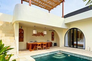Una cocina moderna al aire libre con piscina, escalones de piedra y una zona de estar cubierta.