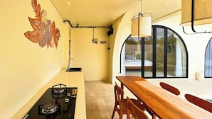 A modern kitchen with a gas stove, wooden dining table, and chairs. There is a decorative wall art and a window with a view of the outdoors. - Esha Private Pool Villas by AGATA (Ungasan)