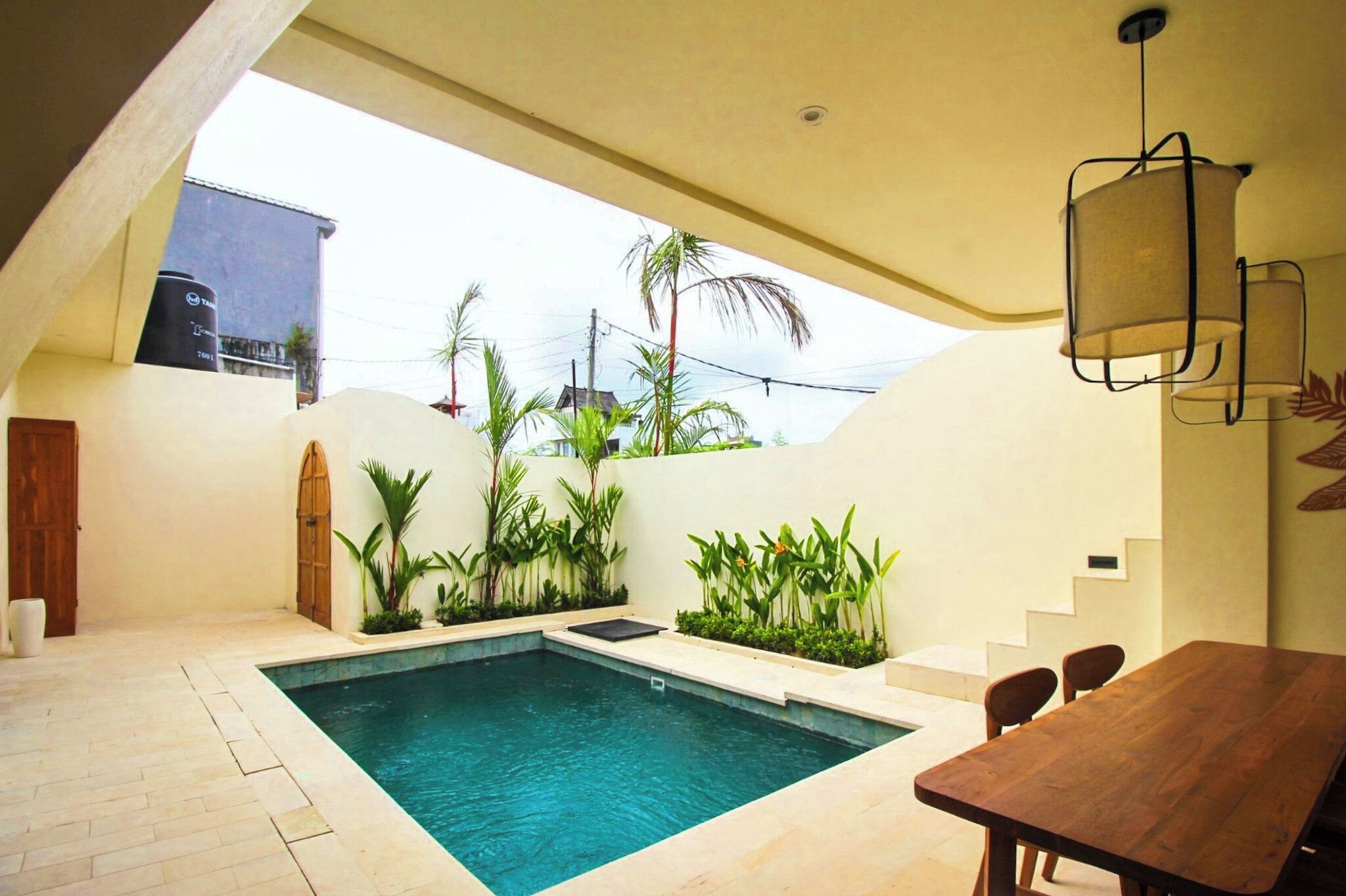 A swimming pool with a wooden table and chairs, surrounded by plants and a staircase.