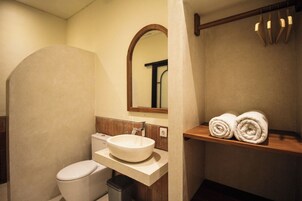 Un baño con un lavamanos blanco, un inodoro y un espejo. Hay dos toallas en un estante.
