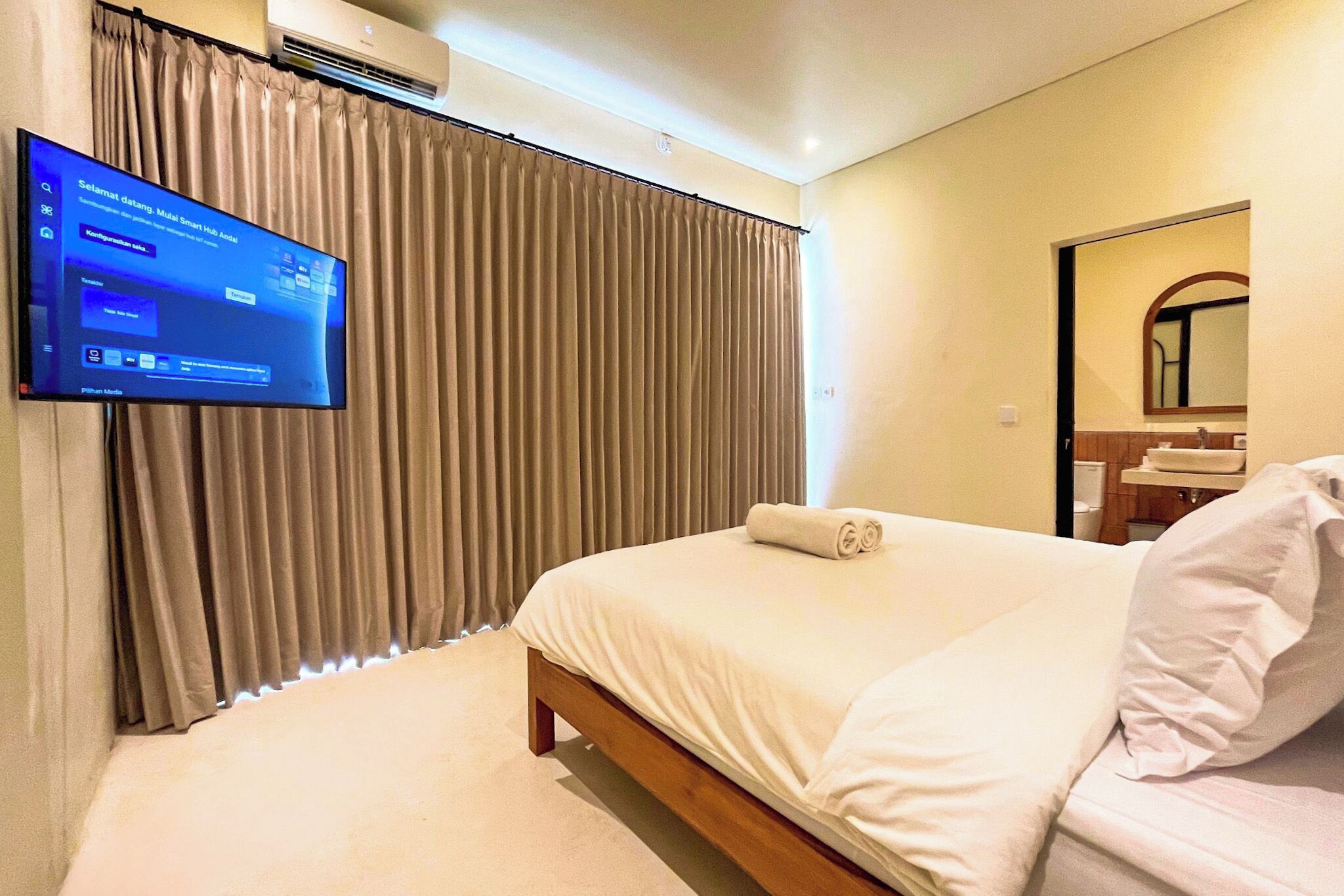 Een hotelkamer met een bed, een aan de muur bevestigde televisie en een raam met gordijnen.