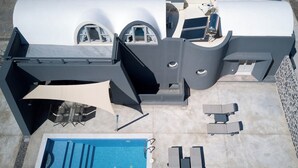 Ovenudblik over et moderne poolområde udendørs, med et integreret spabad, liggestole og et overdækket siddeområde.