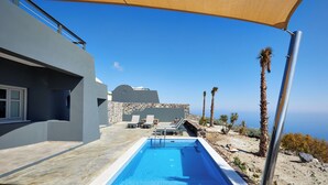 Area piscina moderna con vista aperta sul mare, pareti in pietra e lettini da relax.