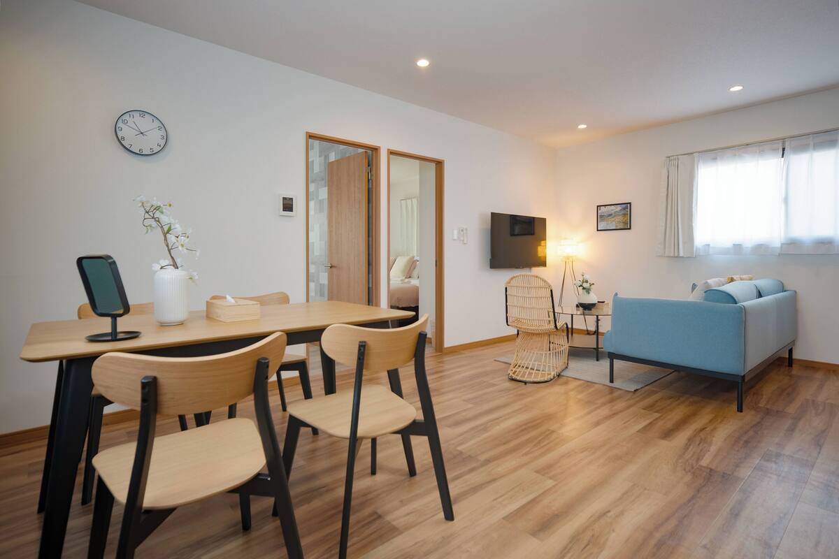 A modern living room with a dining area, a sofa, a TV, and a clock on the wall.
