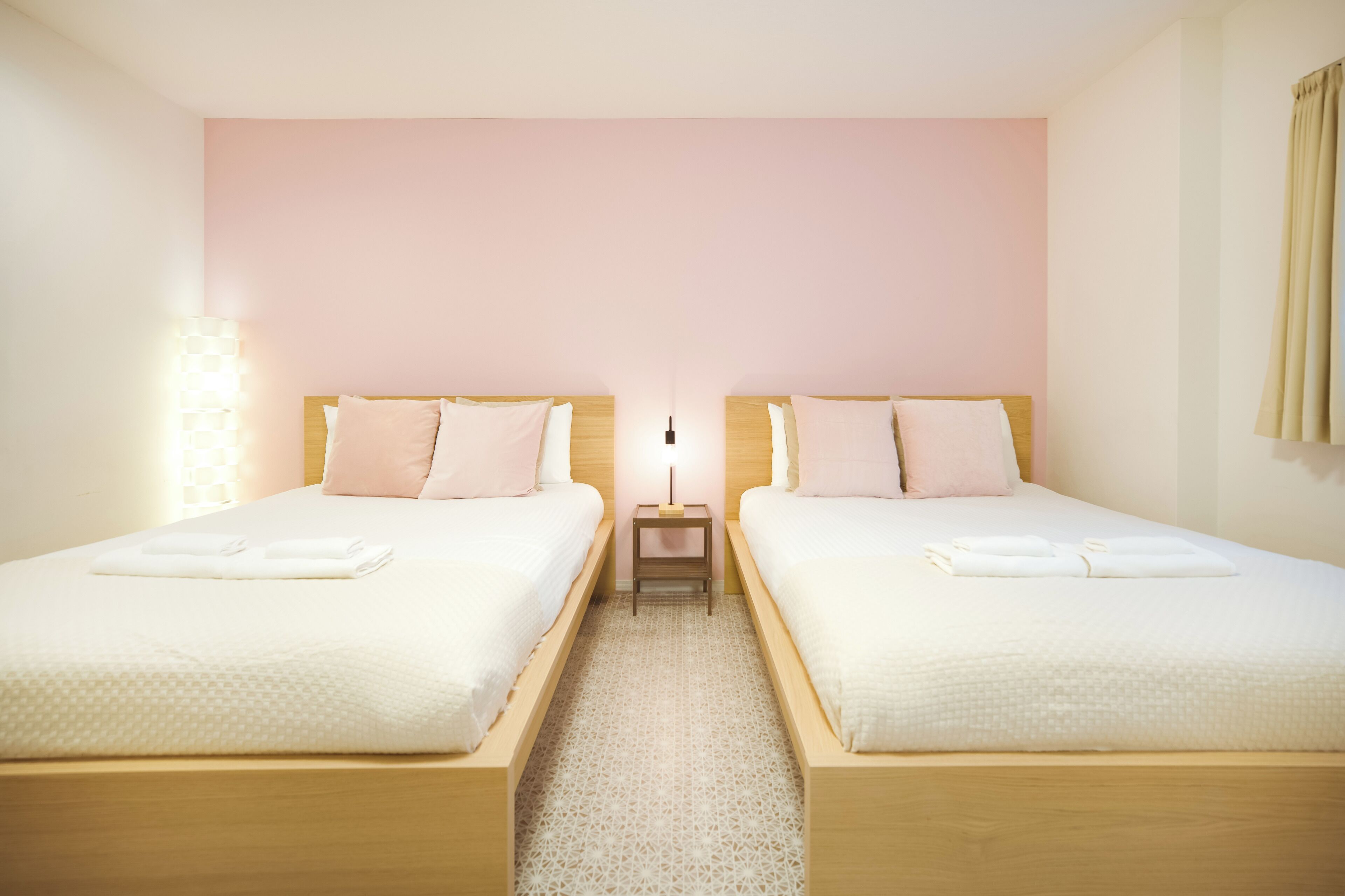 A hotel room with two beds, a nightstand, and a wall-mounted lamp.