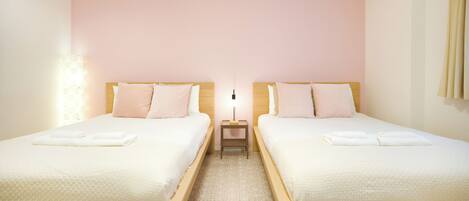 A hotel room with two beds, a nightstand, and a wall-mounted lamp.