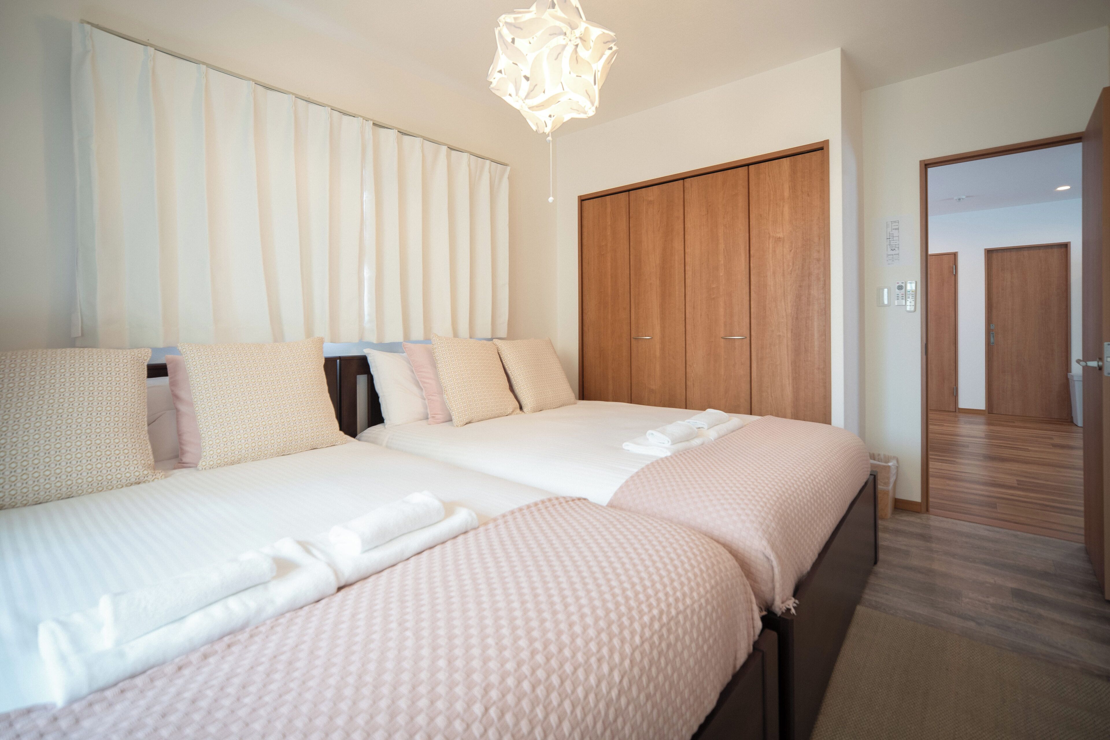 Une chambre d’hôtel avec deux lits, une armoire en bois et un lustre moderne.