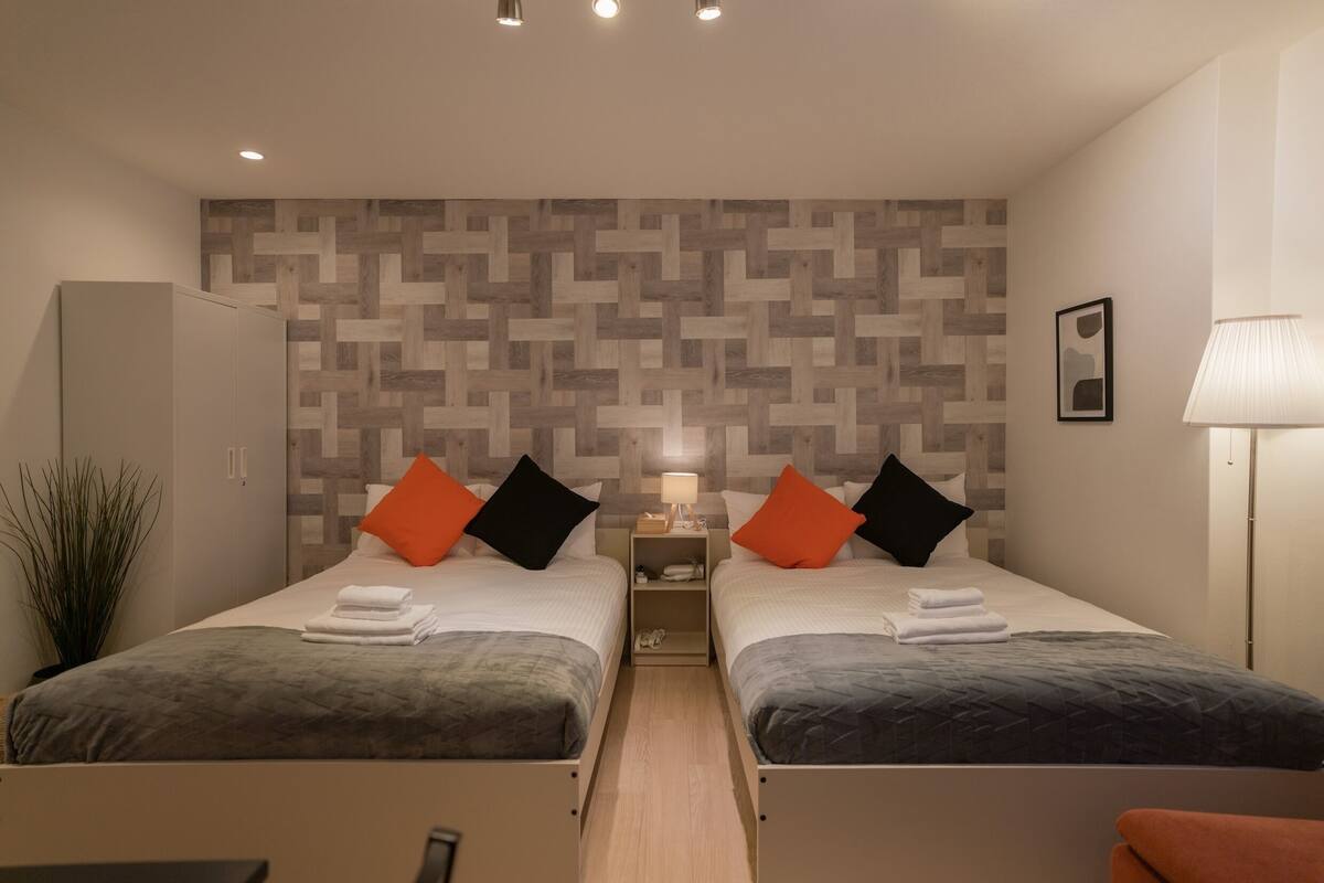 A twin room with two beds, a nightstand, a lamp, and a wall with a geometric pattern.