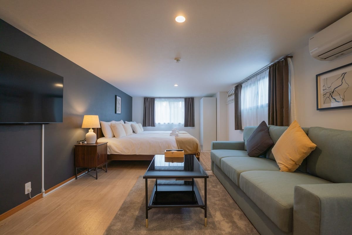 A modern hotel room with a bed, a sofa, a TV, and a desk.