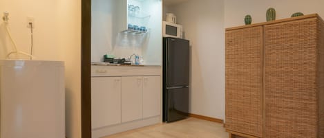 A kitchen with a white refrigerator, a black double-door refrigerator, and a wicker cabinet with decorative cacti.