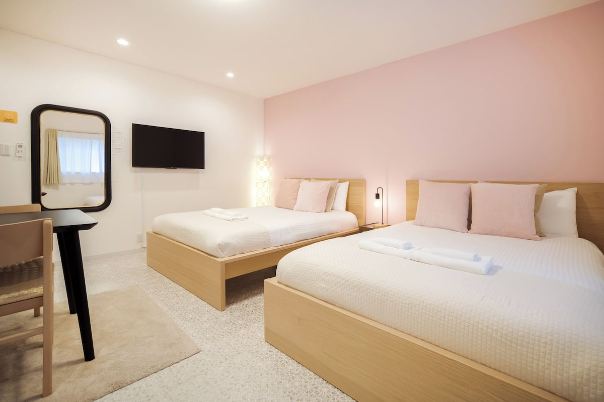 A hotel room with two beds, a desk, a chair, a flat-screen TV, and a mirror.
